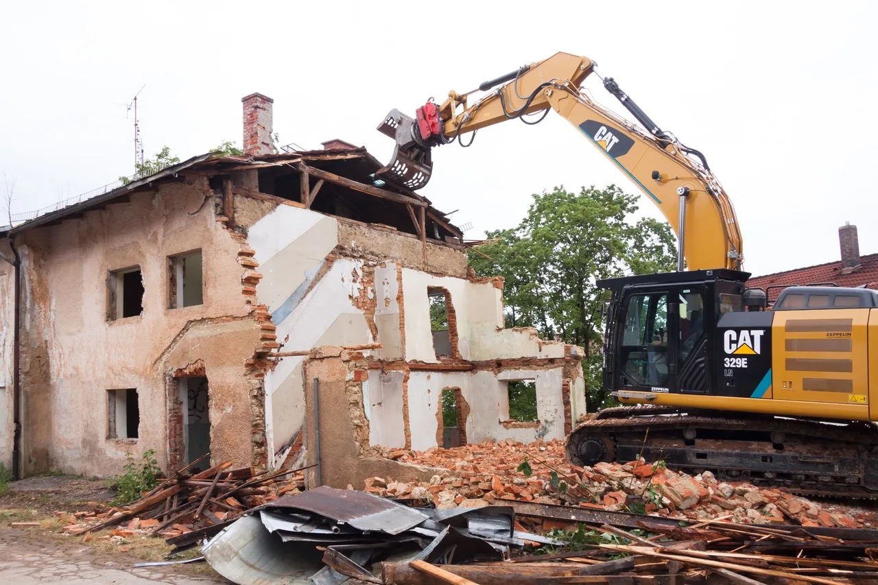 Demolition of an old building with a Caterpillar excavator, rubble, and debris in progress.