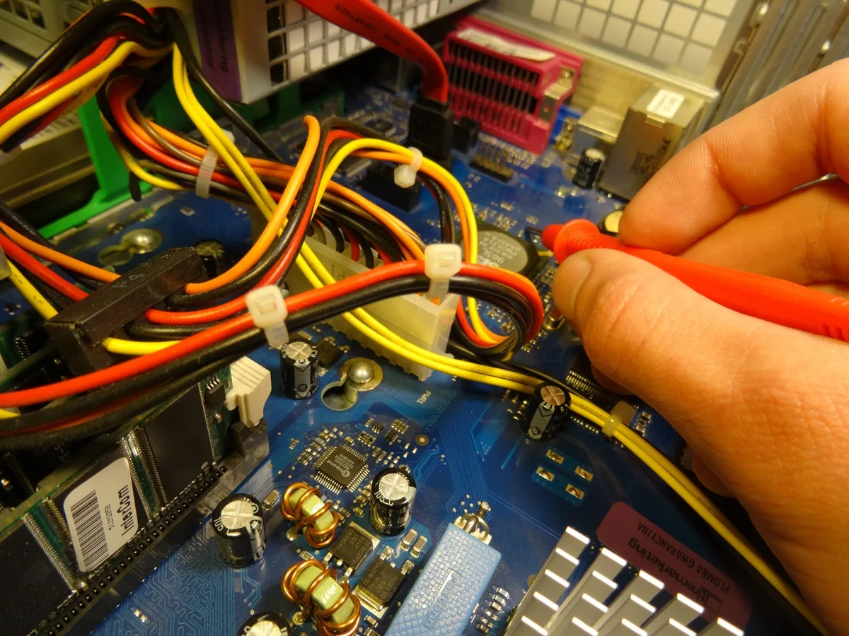 Hands repairing computer interior with multicolored cables on blue motherboard.