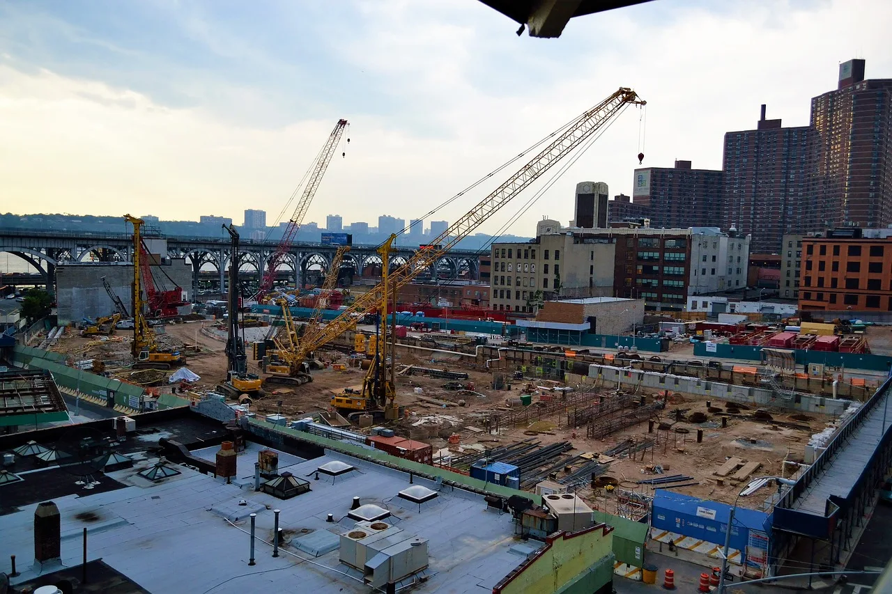 Construction site with cranes in an urban cityscape, high-rise buildings in the background.